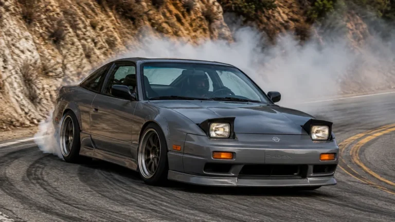 Nissan 240 SX grise en drift sur une route de montagne avec fumée de pneus.
