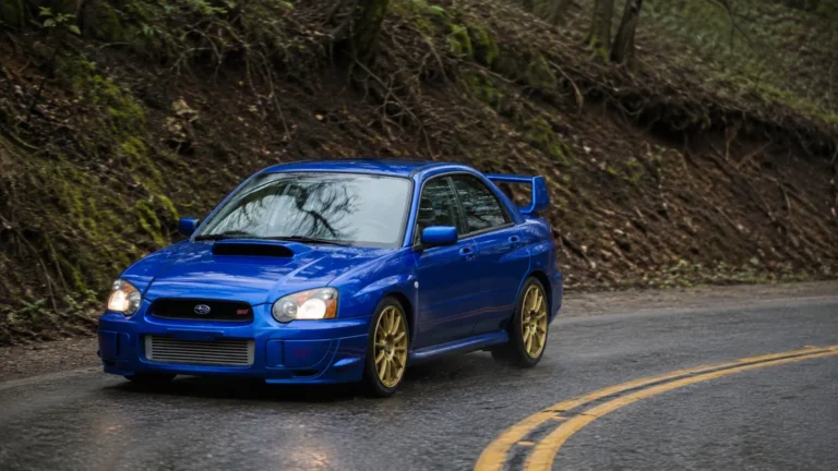 Subaru Impreza WRX STI bleue roulant sur une route de montagne humide et sinueuse.