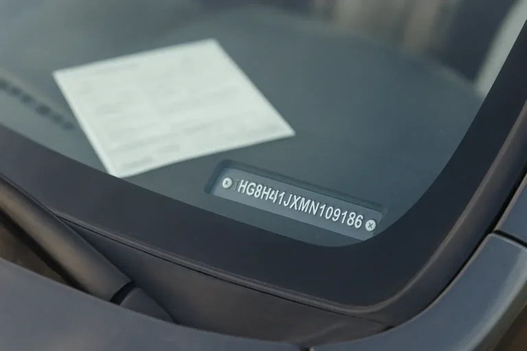 Gros plan sur le VIN visible au bas du pare-brise d’une voiture, avec une carte grise floue en arrière-plan