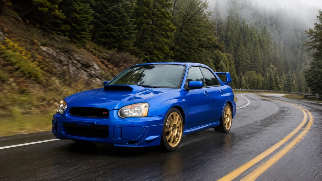 WRX STI Impreza bleue roulant sur une route de montagne humide au cœur d’une forêt.